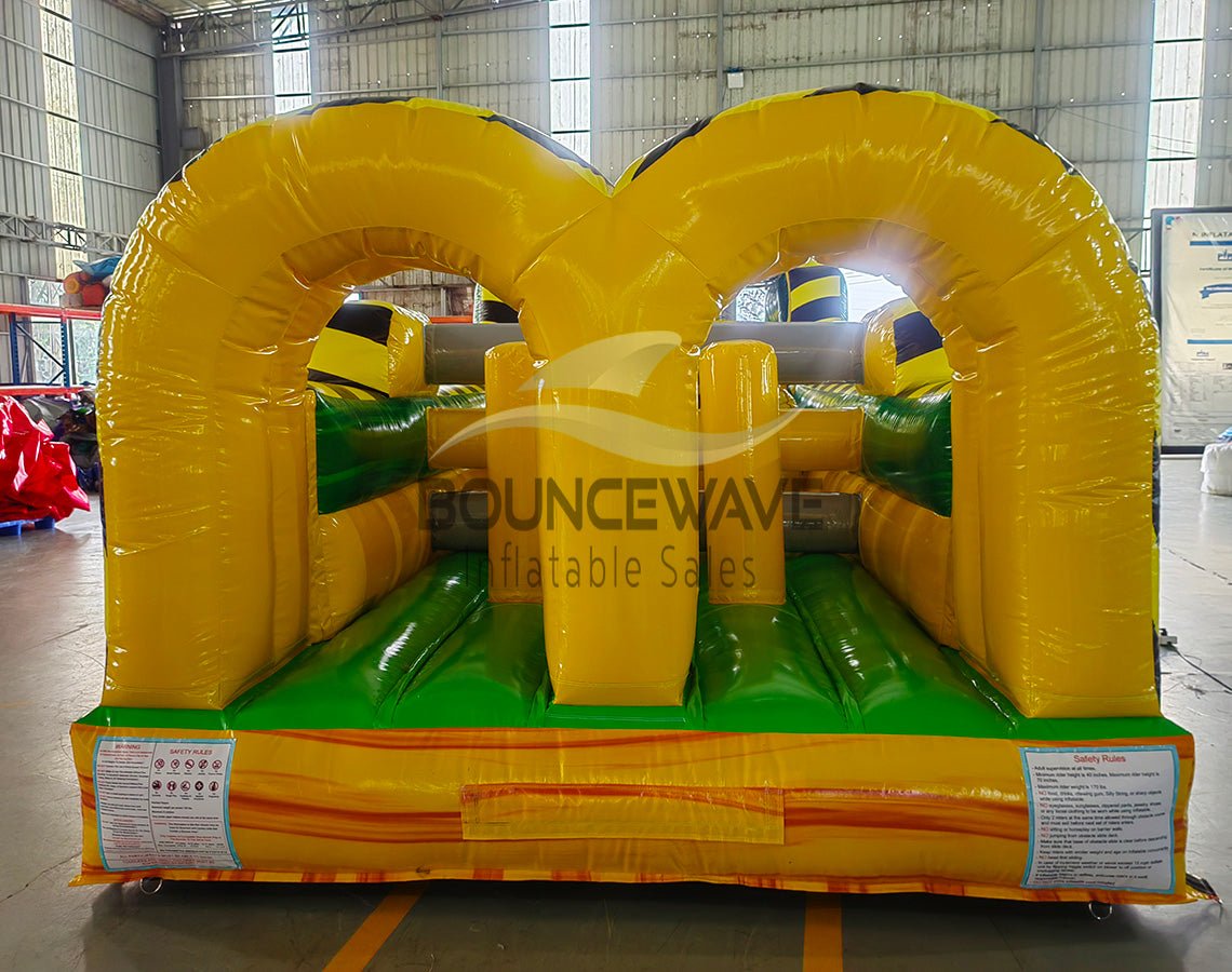 46ft Toxic Open Air Hybrid Inflatable Obstacle Course front view highlighting yellow and black caution-themed design, arched entrances, and green floor in indoor facility
