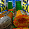 Interior view of 53ft XL Radioactive Run Commercial Hybrid Inflatable Obstacle Course showing inflatable obstacles. The image displays yellow and gray cylindrical barriers, green flooring, and yellow and black striped walls. Various inflatable obstacles are visible, demonstrating the course's challenging layout.