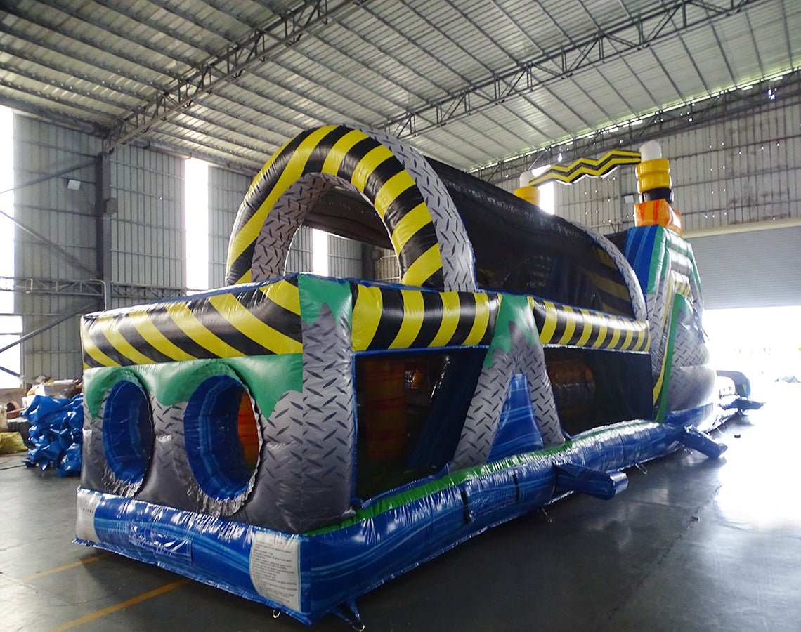 cross rear view of 53ft XL Radioactive Run Commercial Hybrid Inflatable Obstacle Course showing inflatable obstacles. The image displays yellow and gray cylindrical barriers, green flooring, and yellow and black striped walls. Various inflatable obstacles are visible, including tunnels and climbing areas, demonstrating the course's challenging layout.