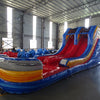 Front view of 53ft XL Rip Curl Commercial Hybrid Inflatable Obstacle Course showing dual red slides and a blue and yellow base. The inflatable features multiple obstacles, tunnels, and a large circular splash pool. Various other inflatable products and equipment are visible in the warehouse background.
