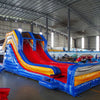 Close-up view of 53ft XL Rip Curl Commercial Hybrid Inflatable Obstacle Course entrance area. Features a blue and yellow color scheme with red accents, dual circular entrances, and a large arched top with wave designs. Safety instructions are visible on the front panel. Set up in a warehouse with other inflatable products in the background.
