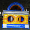 Three-quarter rear view of 53ft XL Rip Curl Commercial Hybrid Inflatable Obstacle Course displaying its full length. The structure has a blue and yellow design with dual red slides, multiple obstacles, and a large circular splash pool. Various other inflatable products and warehouse equipment are visible, showcasing its size and commercial setting.
