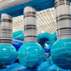 62ft Bahama 2-Piece Wet/Dry Inflatable Obstacle Course featuring large inflatable pillars with striped design and turquoise base in warehouse setting
