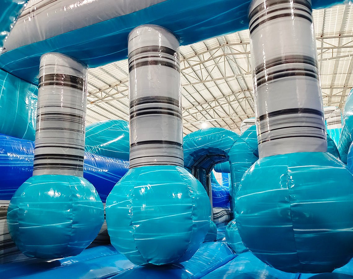 62ft Bahama 2-Piece Wet/Dry Inflatable Obstacle Course featuring large inflatable pillars with striped design and turquoise base in warehouse setting
