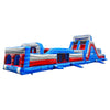 Large inflatable obstacle course with red, blue, and gray color scheme. Features multiple sections including climbing walls, slides, tunnels, and obstacles. Set up in an indoor warehouse with metal roofing visible, surrounded by other inflatable products and equipment.