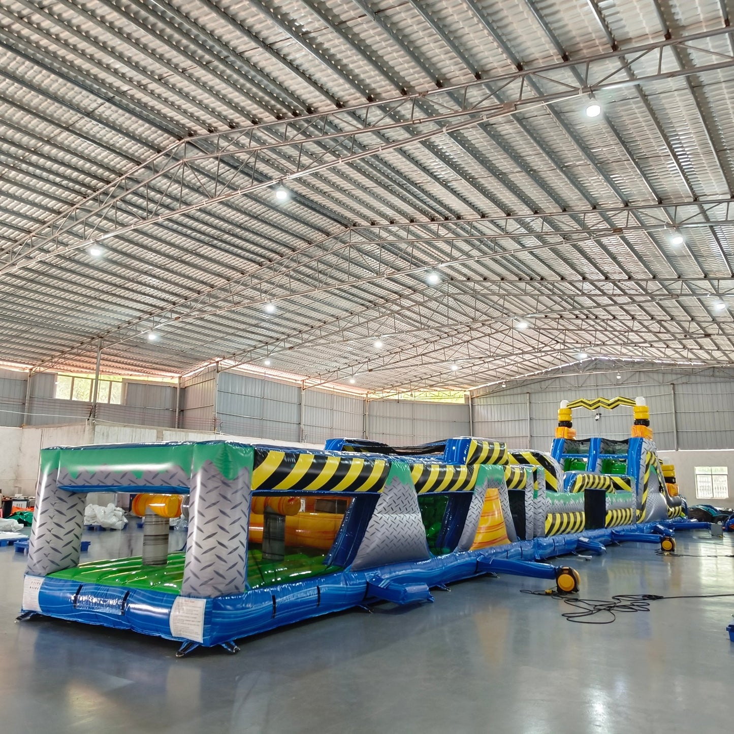 92ft Radioactive Run 3-Piece Wet/Dry Inflatable Obstacle Course angled view displaying yellow and black design, multiple inflatable obstacles, and blue base in indoor facility
