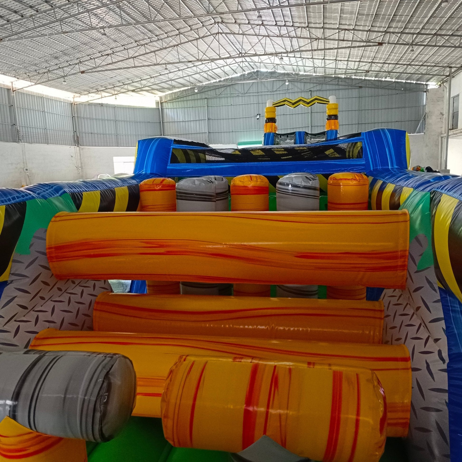 92ft Radioactive Run 3-Piece Wet/Dry Inflatable Obstacle Course front view showcasing yellow and black hazard-themed structure with dual green slides, inflatable barrels, and blue base in warehouse setting
