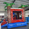 Inflatable tropical-themed combo featuring a bounce house with palm tree decorations, attached slide, and splash pool. The structure has vibrant red, blue, and white colors with inflatable palm trees. Set up in an indoor warehouse with metal roofing and other equipment visible in the background.