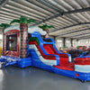 Inflatable tropical-themed combo featuring a bounce house with palm tree decorations, attached slide, and splash pool. The structure has vibrant blue, red, and white colors with brown palm tree trunks. Set up in an indoor warehouse with metal roofing visible.