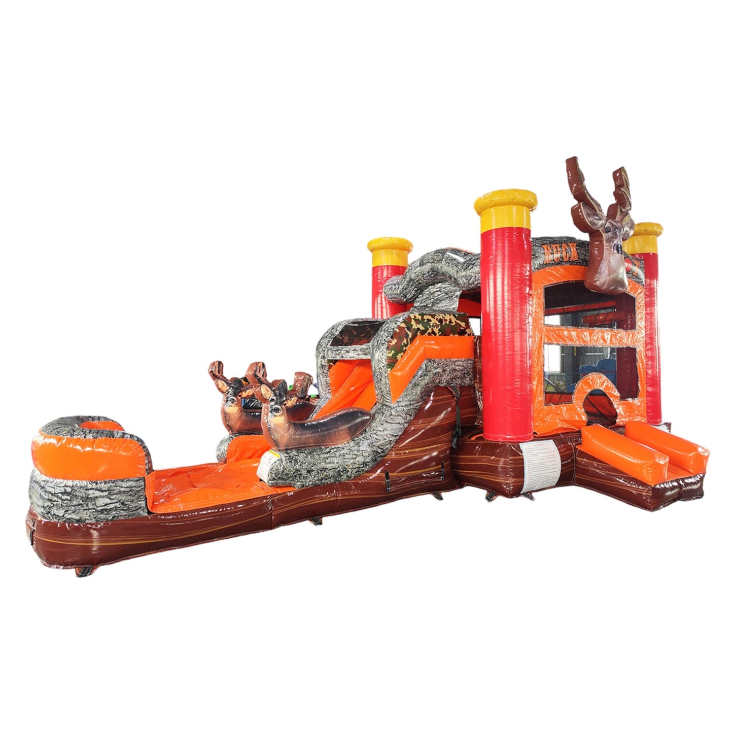 Large inflatable hunting-themed combo featuring a bounce house with deer head decoration, attached slide, and obstacles. The structure has vibrant orange, red, and brown colors with a "BUCK SHOT" banner. Set up in an indoor warehouse with metal roofing visible.