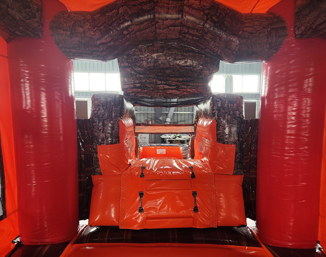 Large inflatable hunting-themed combo featuring a bounce house with deer head decoration, attached slide, and obstacles. The structure has vibrant orange, red, and brown colors with a "BUCK SHOT" banner. Set up in an indoor warehouse with metal roofing and other inflatable products visible in the background.