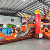 Angled view of the Buck Shot Econo Combo featuring an orange and brown bounce house with deer decorations, red pillars, and tree trunk obstacles. The inflatable is set up in an indoor warehouse with other inflatable products and equipment visible around it.