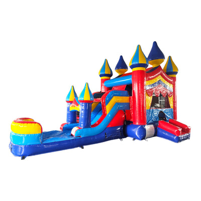 Large inflatable carnival-themed combo featuring a bounce house with colorful spires, attached slide, and splash pool. The structure has vibrant red, blue, and yellow colors with multiple castle-like turrets. Set up in an indoor warehouse with other inflatable products visible.