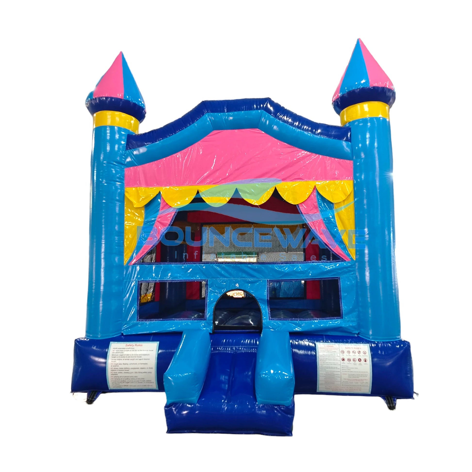 Close-up front view of Carnival Pink Commercial Grade Bounce House isolated on a white background. Shows detailed castle design with blue walls, pink accents, and yellow trim. Three turrets with blue and pink conical tops are prominent. Features a yellow scalloped awning over the entrance, mesh windows, and a blue slide on the side.