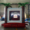 Large inflatable tropical-themed combo featuring a bounce house with palm tree decorations, attached slide, and splash pool. The structure has vibrant red and white colors with brown palm tree trunks. Set up in an indoor warehouse with metal roofing and other inflatable products visible in the background.