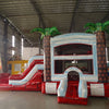 Front view of Crimson Bay Econo Combo, showcasing the bounce house entrance with palm tree decorations, red slide, and white splash pool area. Set up in an indoor facility with other inflatable products and equipment visible in the background.