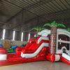 Side angle view of the Crimson Bay Econo Combo featuring a red and white bounce house with palm tree decorations, curved slide, and spacious splash pool. The inflatable is set up in an indoor warehouse with other equipment and inflatables visible.