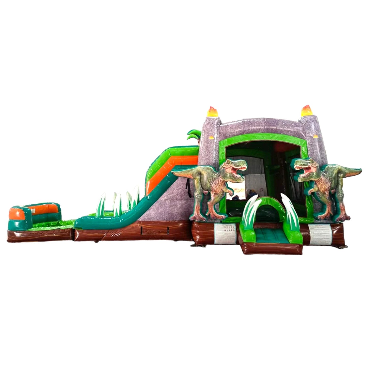 Large dinosaur-themed inflatable combo featuring a gray castle structure with green accents and flame-topped towers. Two realistic T-Rex figures flank the entrance. The combo includes dual slides, a bounce area, and inflatable foliage. Set against a white background, showcasing its prehistoric design for commercial wet/dry use.