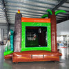 Rear view of Dino Dive Econo Combo highlighting the green bounce house structure with volcano design, orange slide, and splash pool area. Set up in an indoor warehouse with metal ceiling and other inflatable products visible.