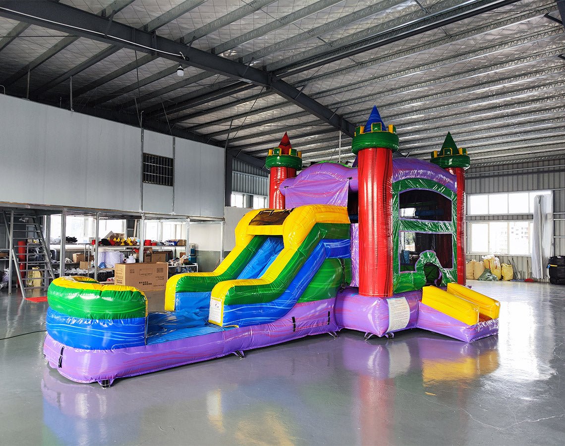 Wide-angle view of the Euro Marble Econo Combo in an indoor warehouse. Highlights the colorful castle-themed inflatable with bounce house, slide, and splash pool. Other inflatable products and warehouse equipment visible in the background.