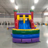 Front view of Euro Marble Dual Lane Commercial Inflatable Combo (Wet/Dry) set up in a large indoor warehouse. Features a castle-themed bounce house with colorful turrets, dual curved slides in red and blue, and a splash pool area. The structure has vibrant purple, yellow, green, and red colors. Metal roofing, concrete flooring, and other warehouse equipment visible in the background.