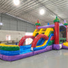 Side view of Euro Marble Dual Lane Commercial Inflatable Combo (Wet/Dry) in a spacious warehouse setting. Showcases the full structure including castle-themed bounce house, dual curved slides in red and blue, and splash pool area. The inflatable features vibrant purple, yellow, green, and red colors. Other inflatable products and warehouse equipment visible, demonstrating its scale in a commercial environment.