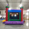 Wide-angle view of Euro Marble Dual Lane Commercial Inflatable Combo (Wet/Dry) set up in a large indoor warehouse. Features a colorful castle-themed structure with red turrets, green battlements, and yellow accents. Two curved slides, one red and one blue, extend from the main structure. The combo includes a bounce house area with mesh windows and a multicolored splash pool at the base. The warehouse setting shows metal roofing, concrete flooring, and other inflatable products in the background.