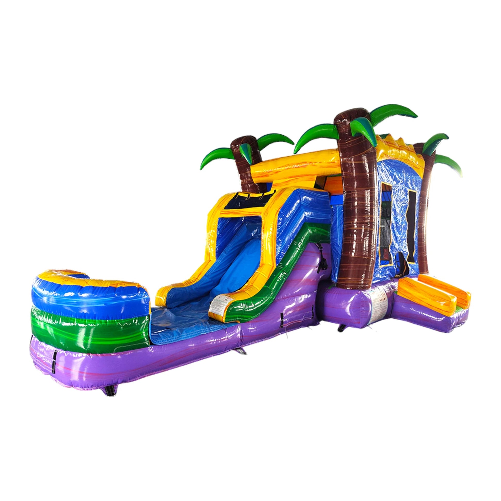 Large inflatable tropical-themed combo featuring a bounce house with palm tree decorations, attached slide, and splash pool. The structure has vibrant blue, yellow, and purple colors with brown palm tree trunks. Set up in an indoor warehouse with metal roofing visible.