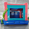 Rear view of Hammerhead Reef Dual Lane Commercial Inflatable Combo (Wet/Dry) featuring a vibrant ocean-themed design. The structure has a pink coral-patterned frame with a teal entrance, dual blue slides, and a large green octopus on top. Inflatable green tentacles with eyes flank the sides. A blue wave-patterned splash pool is visible at the base. Set up in a large indoor warehouse with metal roofing and various other inflatable products visible in the background.