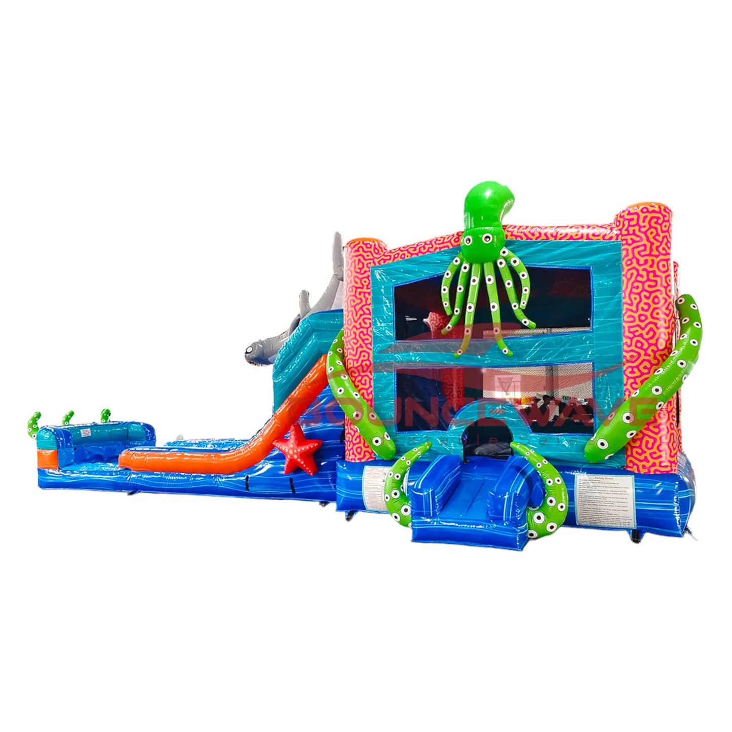 Side view of Hammerhead Reef Dual Lane Commercial Inflatable Combo isolated on a white background. The inflatable features dual blue slides, a large green octopus, inflatable shark fins, and a pink coral-patterned structure. The combo showcases its underwater theme with a bounce house area and splash pool, highlighting its design for commercial wet/dry use.