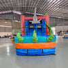 Close-up front view of Hammerhead Reef Dual Lane Commercial Inflatable Combo showing the entrance area. Features a pink coral-patterned structure with mesh windows, inflatable shark fins, and a large green octopus on top. The dual blue slides and splash pool are partially visible. Set in a warehouse with concrete flooring and various other inflatable products in the background, showcasing its commercial use context.