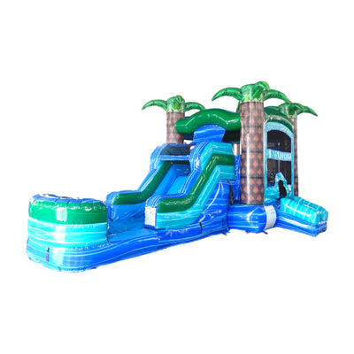 Large inflatable tropical-themed combo featuring a bounce house with palm tree decorations, attached slide, and splash pool. The structure has vibrant blue and green colors with brown palm tree trunks. Set up against a white background.