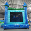 Rear view of Island Drop Splash & Save Dual Lane Inflatable Combo (Wet/Dry) set up in a large indoor warehouse. The inflatable features blue castle-like towers with conical tops, a turquoise bounce house area with mesh windows, and dual blue water slides. A green trim adorns the top, and a blue splash pool is visible at the base. The warehouse setting shows a metal roof with bright lighting, and various other inflatable products can be seen in the background.