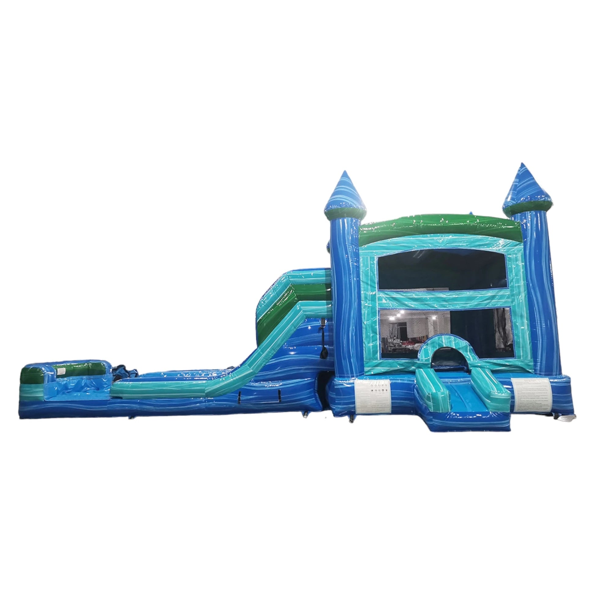 Side view of Island Drop Splash & Save Dual Lane Inflatable Combo featuring blue castle-like towers with conical tops, dual water slides, and a turquoise bounce house area. The structure includes a green trim and a blue splash pool base. Set against a white background, showcasing its design for commercial wet/dry use.