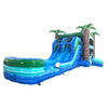 Side view of Island Drop Dual Lane Commercial Inflatable Combo isolated on a white background. The inflatable features dual blue water slides, green inflatable palm trees, a climbing wall, and a large splash pool. The combo showcases its tropical theme with a blue and green color scheme, highlighting its design for commercial wet/dry use.