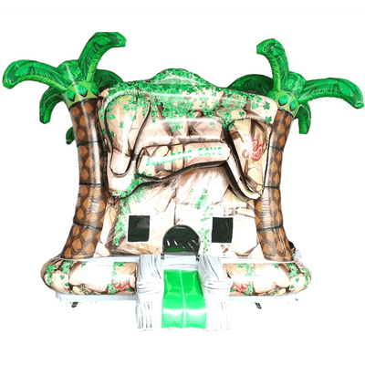 Tropical-themed inflatable Jurassic Cave Commercial Grade Bounce House featuring a tan cave-like structure with green inflatable palm trees on each side. The entrance resembles a cave opening with faux rock textures and green vines. A small slide protrudes from the front, and mesh windows allow visibility inside. The bounce house is set against a white background, showcasing its prehistoric jungle design suitable for commercial use.