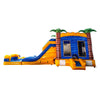 side view of Lava Falls Dual Lane Commercial Inflatable Combo featuring a vibrant volcano theme. The structure has dual blue water slides, orange and yellow lava-like patterns, and inflatable palm trees. A blue bounce house area with mesh windows is visible. Set up in a large indoor warehouse with metal roofing and other inflatable products in the background.