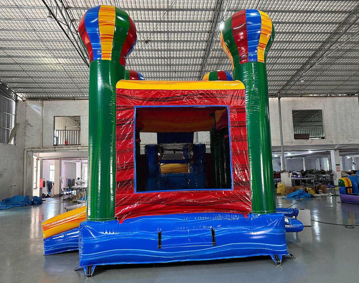 Front view of Marble Balloon Econo Combo, showcasing the bounce house entrance with colorful hot air balloon decorations, slide, and splash pool area. Set up in an indoor facility with other inflatable products and equipment visible in the background.