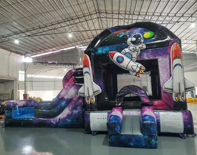 Side view of MoonWalker Commercial Econo Inflatable Wet/Dry Combo showing space-themed inflatable with cosmic patterns, slide, and play area. Features vibrant purple, blue, and pink colors with astronaut and rocket designs. Set up in a spacious indoor warehouse.