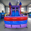 Front view of Multi Color Marble Splash & Save Dual Lane Inflatable Combo showing dual blue slides, purple castle towers with conical tops, and a colorful splash pool area. Set up in a warehouse with concrete flooring, metal roofing, and various other inflatable products and equipment visible in the background.