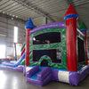 Cross Rear view of Multi Color Marble Splash & Save Dual Lane Inflatable Combo set up in a large indoor warehouse. The inflatable features colorful castle towers, dual slides, and a bounce house area with mesh windows. A green panel with white designs is visible on one side. Metal roofing and various inflatable products are visible in the background.