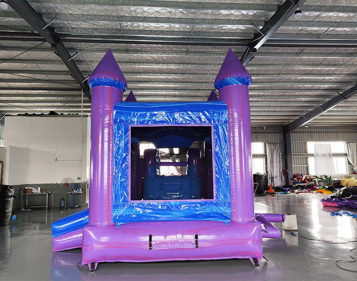 Close-up front view of Mystic Castle Commercial Econo Inflatable Combo (Wet/Dry) highlighting the entrance with purple turrets, blue walls, and yellow accents. Mesh windows and interior obstacles visible. Displayed in an indoor warehouse setting, emphasizing its detailed design and commercial-grade construction.