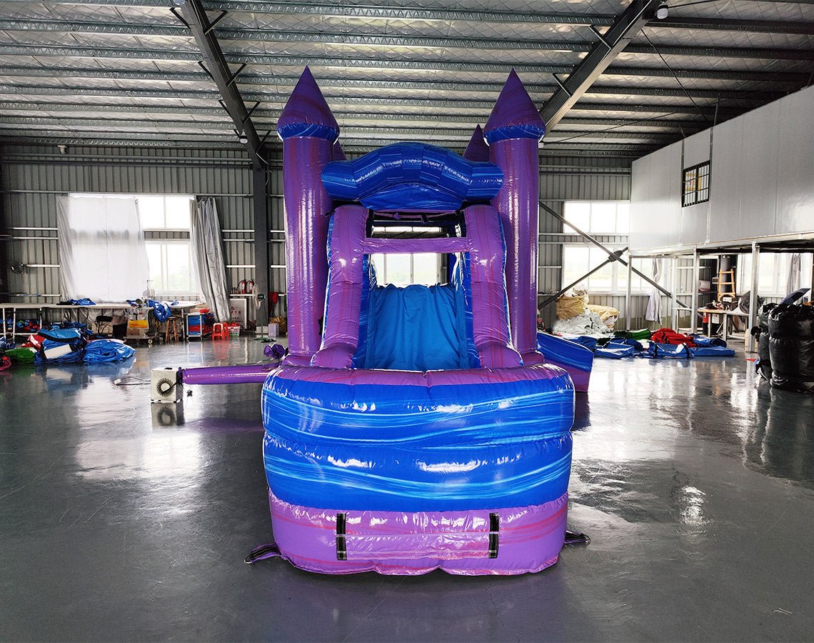 Front view of Mystic Castle Commercial Econo Inflatable Combo (Wet/Dry) showing the bounce house entrance with purple turrets and blue frame. Interior visible through mesh windows. Set up in an indoor warehouse with concrete flooring, showcasing its vibrant colors and castle-like design.