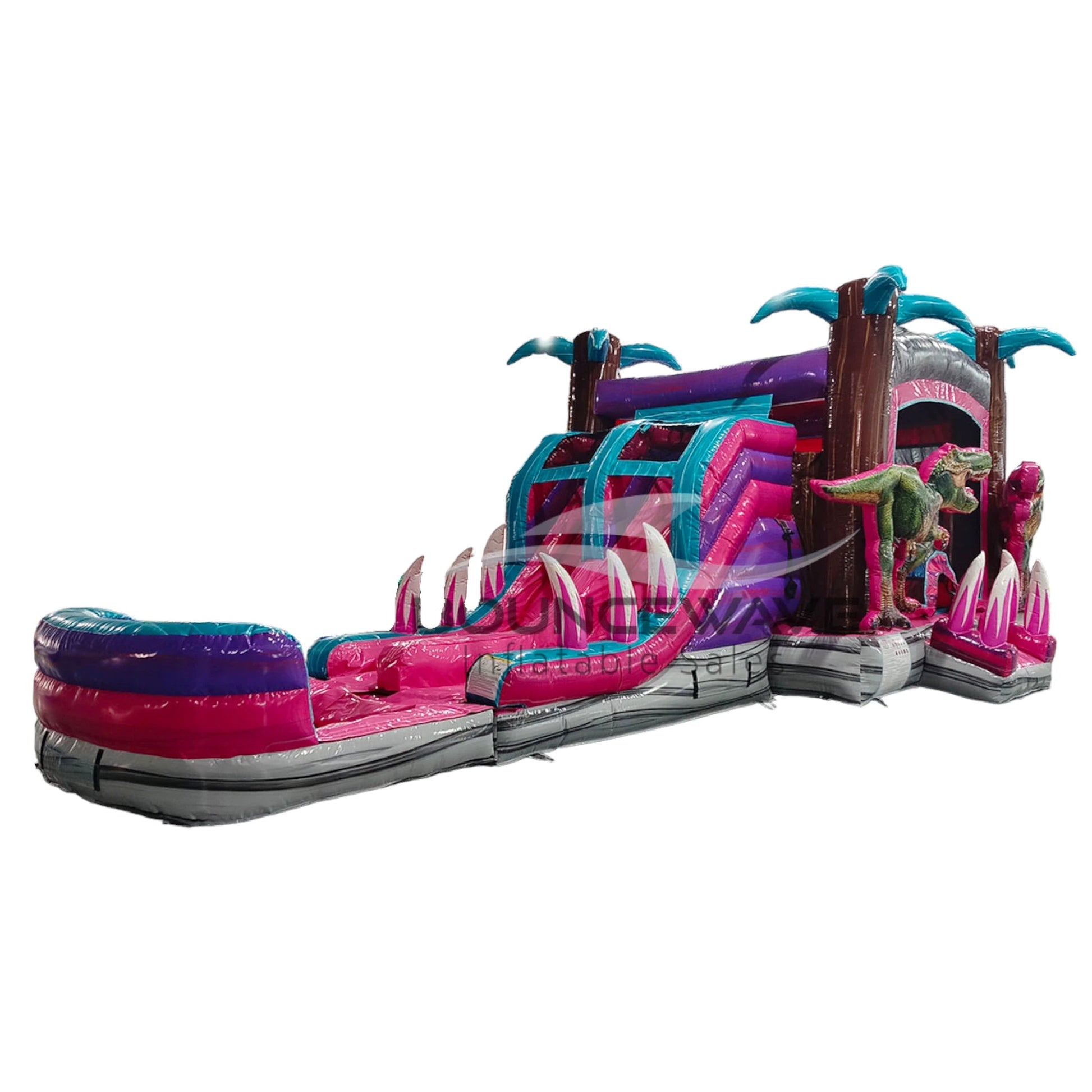 Side view of Pink Dino Dive Dual Lane Commercial Inflatable Combo isolated on a white background. The inflatable features dual slides in pink and blue, a purple and pink structure with palm tree accents, and realistic green dinosaur figures. The design showcases its prehistoric theme for commercial wet/dry use.