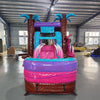 Front view of Pink Dino Econo Combo, showcasing the bounce house entrance with palm tree decorations, dinosaur figures, pink slide, and purple splash pool area. Set up in an indoor facility with other inflatable products and equipment visible in the background.