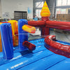 Close-up view of Primary Marble Toddler Bounce House interior, showing colorful inflatable obstacles including yellow and blue cylindrical pillars, a red arched tunnel, and a blue curved slide. The bounce floor is visible with a blue base. Set in a warehouse environment with metal roofing and windows in the background.