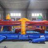 Rear view of Primary Marble Toddler Bounce House showing the blue base, red and maroon walls, and yellow dome top with orange swirl patterns. Four corner towers in various colors visible. Set in a warehouse with metal ceiling, windows, and other inflatable products in the background.