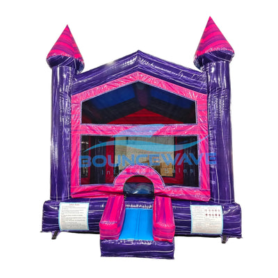 Front view of Purple Palace Commercial Grade Bounce House featuring a vibrant purple and pink color scheme. The inflatable structure has two tall purple towers with pink conical tops, a pink arched entrance, and mesh windows. A small slide protrudes from the front. Set against a white background, showcasing its castle-like design for commercial use.