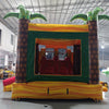 Rear view of Rasta Splash Dual Lane Commercial Inflatable Combo featuring a tropical theme with inflatable palm trees. The structure has dual slides in red and yellow, a green bounce house area with mesh windows, and a colorful base in yellow, green, and red. Set up in a large indoor warehouse with metal roofing and bright lighting visible.