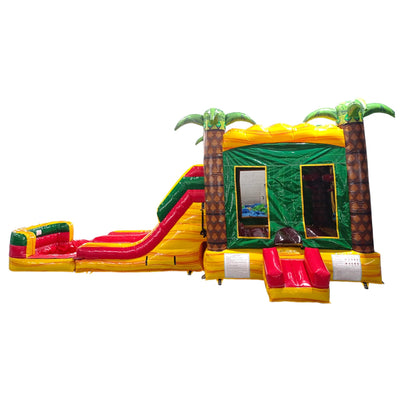 Wide-angle view of Rasta Splash Dual Lane Commercial Inflatable Combo isolated on a white background. The inflatable features dual slides in red and yellow, inflatable palm trees, a green bounce house structure, and a colorful base in yellow, green, and red. The design showcases its tropical theme for commercial wet/dry use.